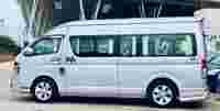 A silver passenger van parked outside a modern building, featuring multiple windows and a sleek design.