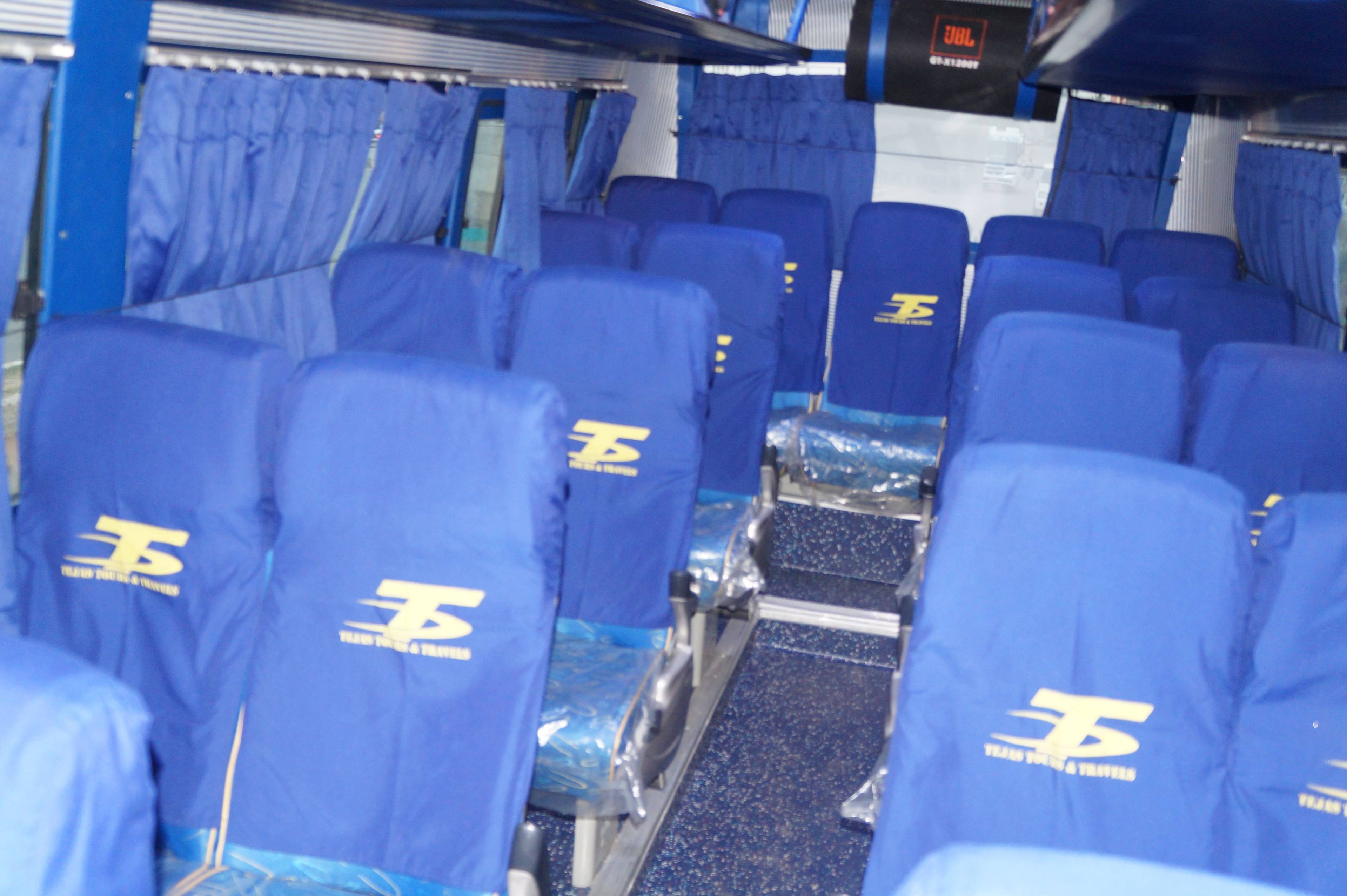 Interior of a bus featuring blue seats with logos, empty rows, and curtains, suggesting a waiting environment.