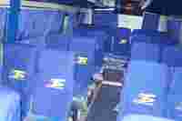 Interior of a bus featuring blue seats with logos, empty rows, and curtains, suggesting a waiting environment.