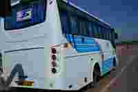 White travel bus with blue stripes parked by the roadside, displaying "Tejas Tours & Travels" on the rear window.