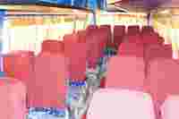 A bus interior with rows of red fabric-covered seats, partially covered in plastic, and golden curtains at the windows.