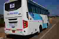 White bus with blue stripes, branded "Tejas Tours & Travels," parked on a roadside with clear skies in the background.