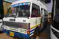 A white SML T3500 bus with blue and yellow stripes is parked next to another bus, with its door slightly open.
