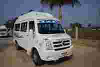 A white traveler van with "TEJAS" on the windshield is parked on a road, surrounded by palm trees and open land.