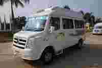A white Force Traveller van parked on a concrete road, palm trees and construction site visible in the background.