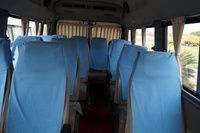 Empty bus interior with rows of seats covered in blue fabric, red carpet on the floor, and light streaming through windows.