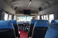 Interior of a van featuring blue seat covers, a TV mounted on the front wall, and a red carpeted floor.