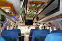 Interior of a minibus featuring blue seat covers, decorative lighting, a ceiling design, and a screen at the front.