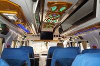 Interior of a minibus featuring blue seat covers, decorative lighting, a ceiling design, and a screen at the front.
