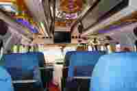 Interior of a spacious, brightly lit vehicle with blue seats, wooden accents, and a mounted screen at the front.