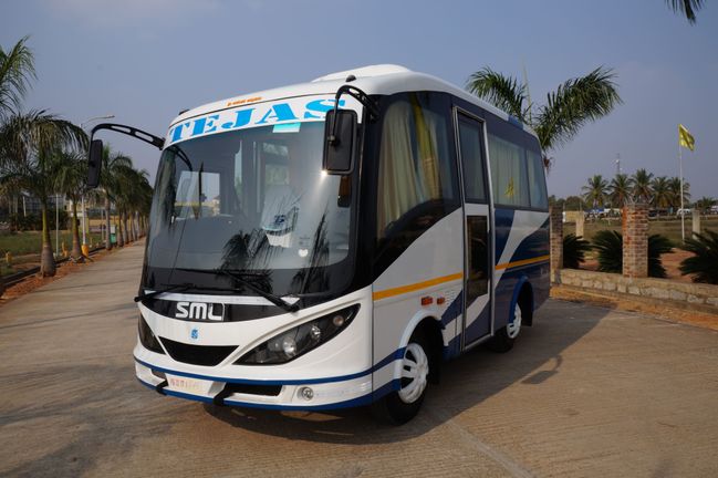 White and blue travel bus parked on a concrete road, surrounded by palm trees and an open landscape in the background.