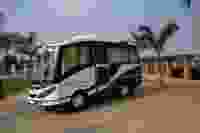 White and blue travel bus parked on a concrete road, surrounded by palm trees and an open landscape in the background.
