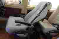 A single light-colored seat with an armrest and seatbelt, placed in a vehicle interior with plush upholstery.
