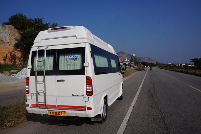 Six white vans and buses parked on a highway under a clear sky, with streetlights along the road.