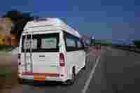 White van parked on the roadside, with a mountain backdrop and a road sign for a café visible ahead.