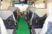Interior view of a vehicle showing beige seats, green carpet, and a front dashboard with a screen. Brightly lit and clean.