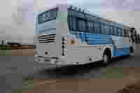 A white bus with blue stripes, labeled "Tejas Tours & Travels," parked on a road with a cloudy sky overhead.