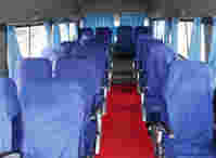 Interior of a bus featuring rows of blue upholstered seats, a red carpet, and light blue curtains along the windows.