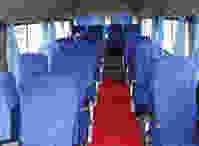 Interior of a bus featuring rows of blue upholstered seats, a red carpet, and light blue curtains along the windows.