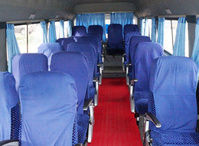 Interior of a bus featuring rows of blue upholstered seats, a red carpet, and light blue curtains along the windows.