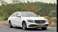 A white Mercedes-Benz S-Class parked on a road, surrounded by greenery and trees in the background.