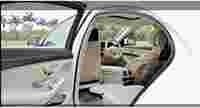 Luxurious car interior with beige leather seats, a steering wheel, and modern controls. Outdoor greenery is visible.
