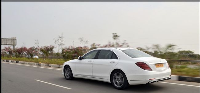 A white Mercedes-Benz S-Class sedan parked on a roadway with greenery in the background.