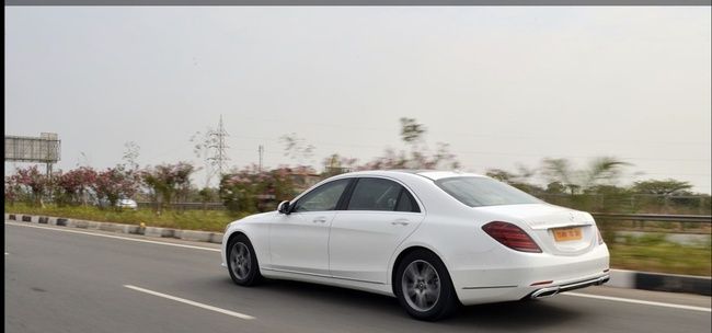 A white Mercedes-Benz S-Class sedan parked on a roadway with greenery in the background.
