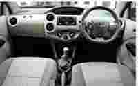 Interior view of a Toyota car featuring a steering wheel, gear shift, and dashboard controls, with fabric seats.