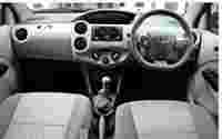 Interior view of a Toyota car featuring a steering wheel, gear shift, and dashboard controls, with fabric seats.