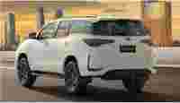 A white Toyota Fortuner driving down a highway with a city skyline and sunset in the background.
