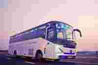 A sleek, modern bus with "TEJA" displayed on its front, parked on a road during sunset with a pastel sky.