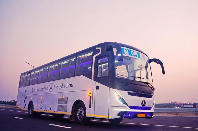 A sleek, modern bus with "TEJA" displayed on its front, parked on a road during sunset with a pastel sky.