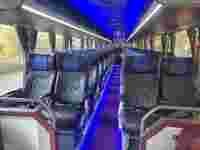 Interior of a luxury bus featuring rows of black and blue patterned seats, with ambient lighting and windows.