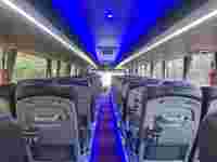 Interior of a modern bus showing rows of black seats, blue LED lighting, and a view through the front windshield.