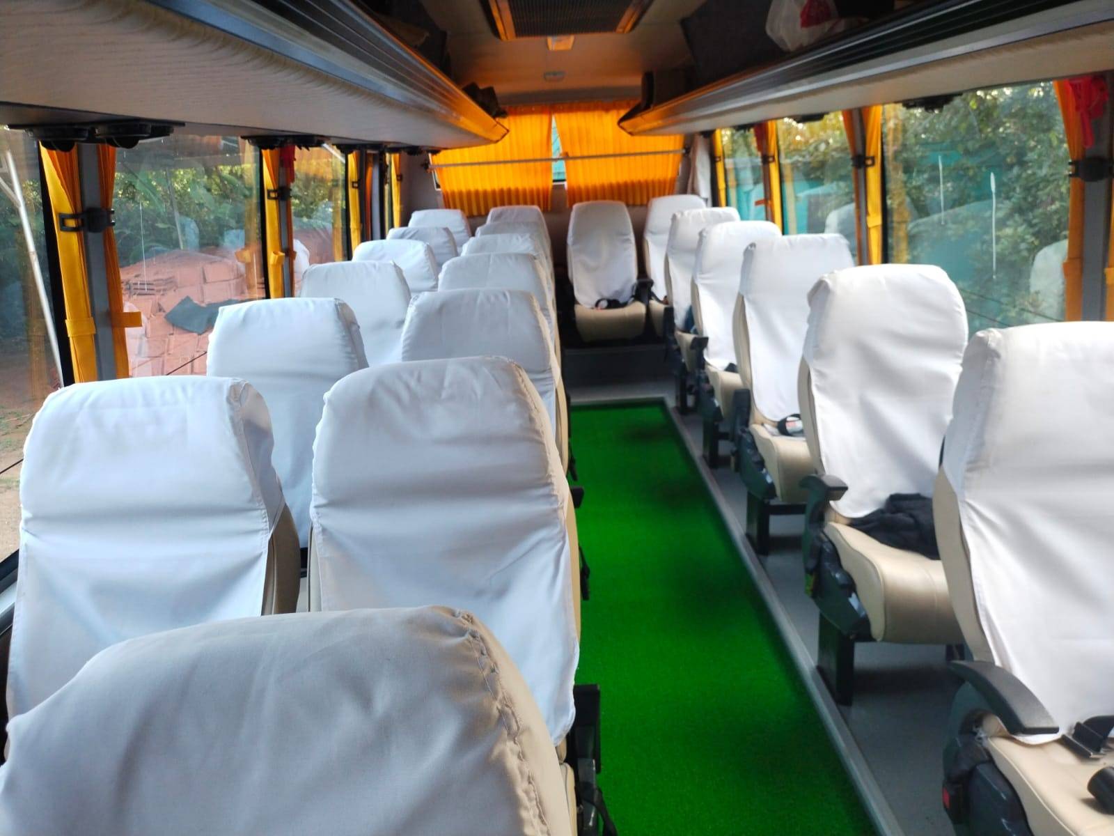 Empty bus interior with rows of covered seats and a green carpeted aisle, illuminated by natural light.