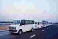 Six white vans and buses parked on a highway under a clear sky, with streetlights along the road.