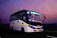 A white and black bus labeled "TEJAS" parked on an empty road under a purple sky, decorated with colorful cushions.