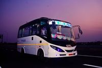 A white and black bus labeled "TEJAS" parked on an empty road under a purple sky, decorated with colorful cushions.