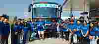 A group of people in blue shirts poses in front of a bus labeled "TEJAS" at a roadside location, showcasing a cheerful atmosphere.