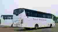 Two white buses parked on an unpaved area, with the phrase "Travel With Dreams" displayed on the rear bus.