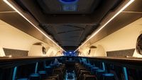 Interior of a bus featuring rows of black seats, overhead lighting, and soft blue ambient light.