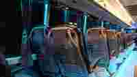 Empty bus interior at night featuring sleek seats with plastic covers and blue ambient lighting.