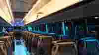 Interior of a modern bus with empty rows of seats, soft blue lighting, and a TV screen at the front.
