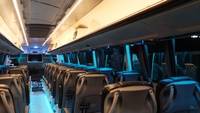 Interior of a modern bus with empty rows of seats, soft blue lighting, and a TV screen at the front.