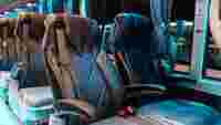 Luxurious black bus seats with armrests, covered in plastic, positioned against a colorful backdrop of illuminated windows.