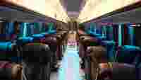 Luxurious bus interior with rows of black leather seats, illuminated by blue lighting, creating a modern, inviting atmosphere.