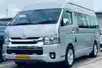 Silver Toyota van parked beside another vehicle, showcasing its large windows and modern design against a cloudy sky.