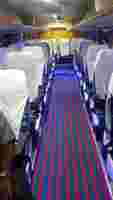 Interior of a bus featuring rows of white-covered seats, vibrant striped carpet, and blue ambient lighting.