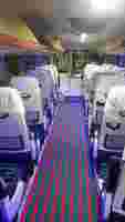 Interior of a bus with white seats, colorful striped carpet, and blue lighting, creating a modern and clean atmosphere.
